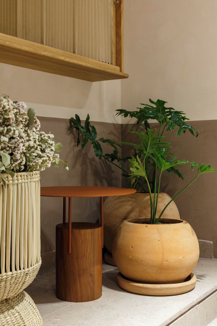 Un rincón de una habitación con una mesa de madera, una cesta de mimbre con flores y una planta en maceta.