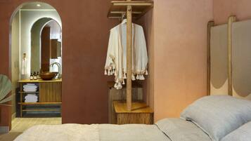 A bedroom with a bed, a wooden shelf with a hanging robe, a wooden stool, and a mirror.