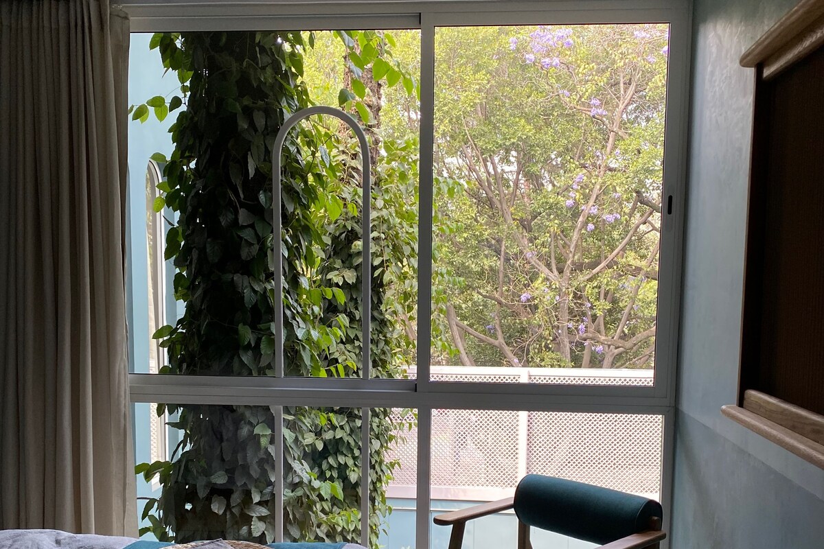 A room with a bed, a chair, and a large window with a view of trees and a building.