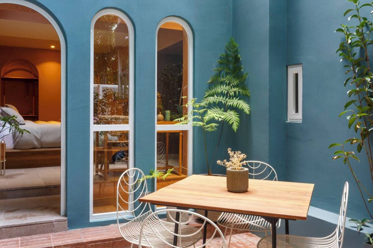 A room with a wooden table and chairs, a potted plant, and a view through a window.