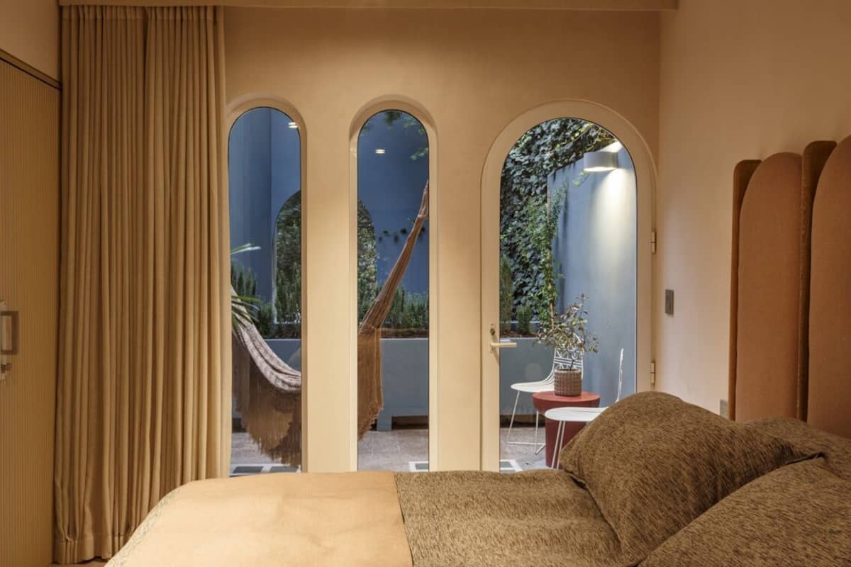 A bedroom with a bed, a view through a set of arched windows to an outdoor area with a hammock and a table.