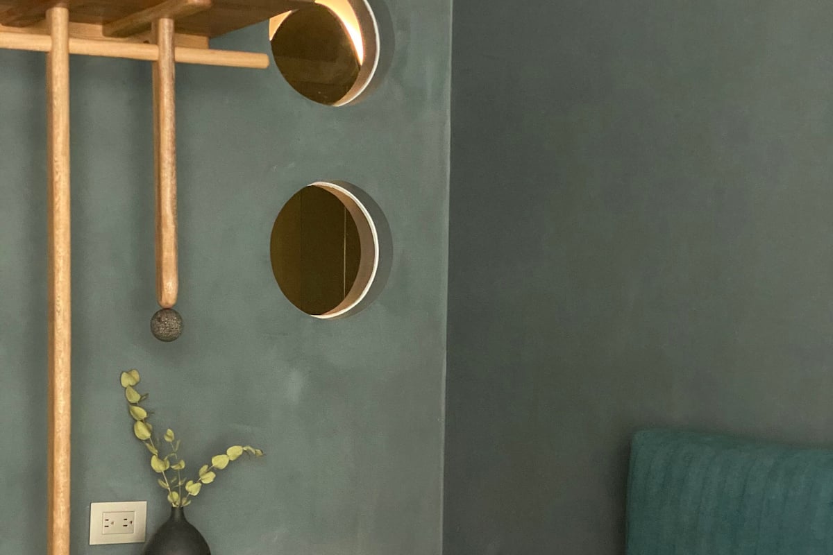 A room with a bed, a wooden cabinet, a small table with a vase, and two wall-mounted mirrors.