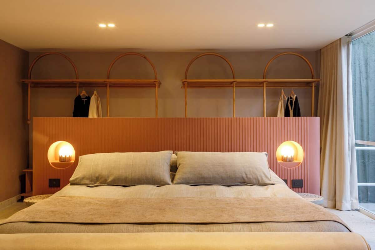 A bedroom with a large bed, two wall-mounted lamps, and a built-in wardrobe with clothing on hangers.