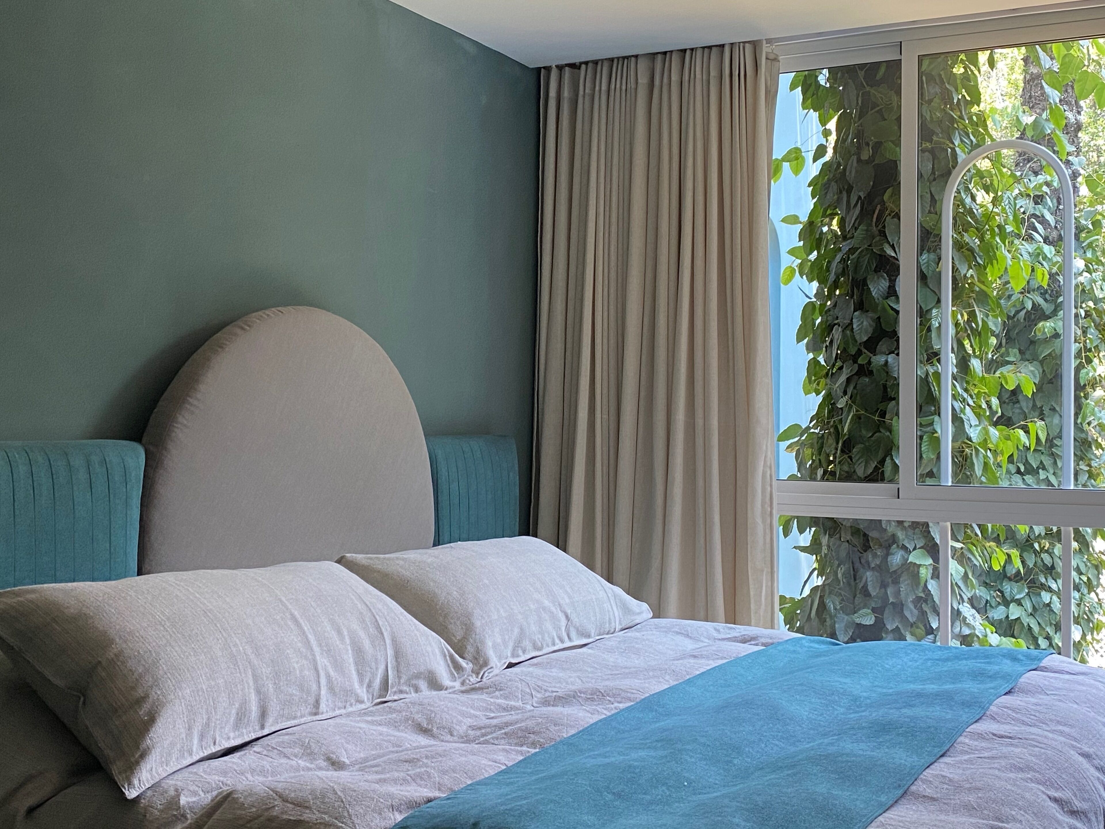 A bedroom with a bed, curtains, and a window with greenery outside.