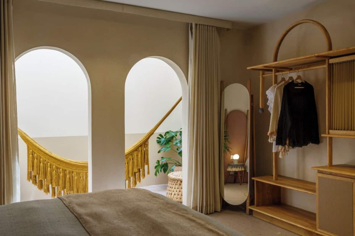A bedroom with a bed, a wardrobe, a mirror, and a hanging chair.
