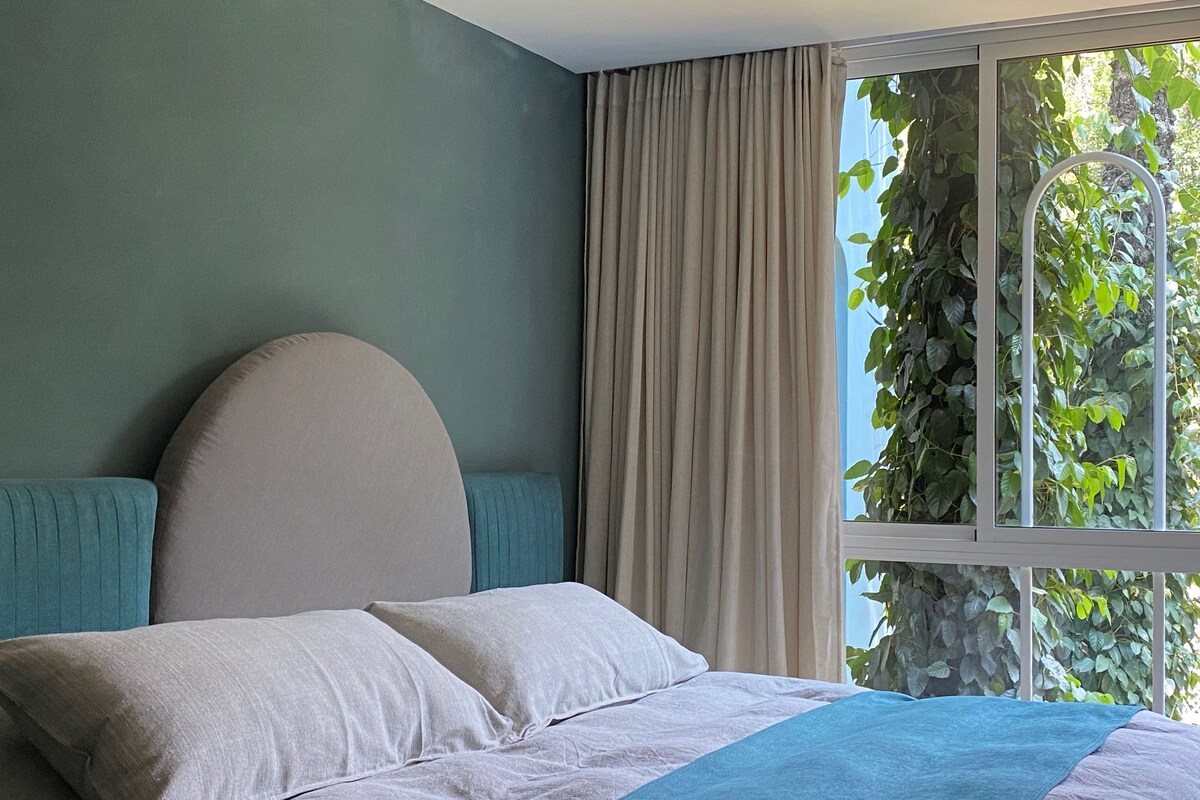 A bedroom with a bed, curtains, and a window with greenery outside.