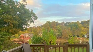 Eine Terrasse mit Tisch und Stühlen, ein Glas Weißwein und Blick auf ein bewaldetes Gebiet mit Häusern im Hintergrund.