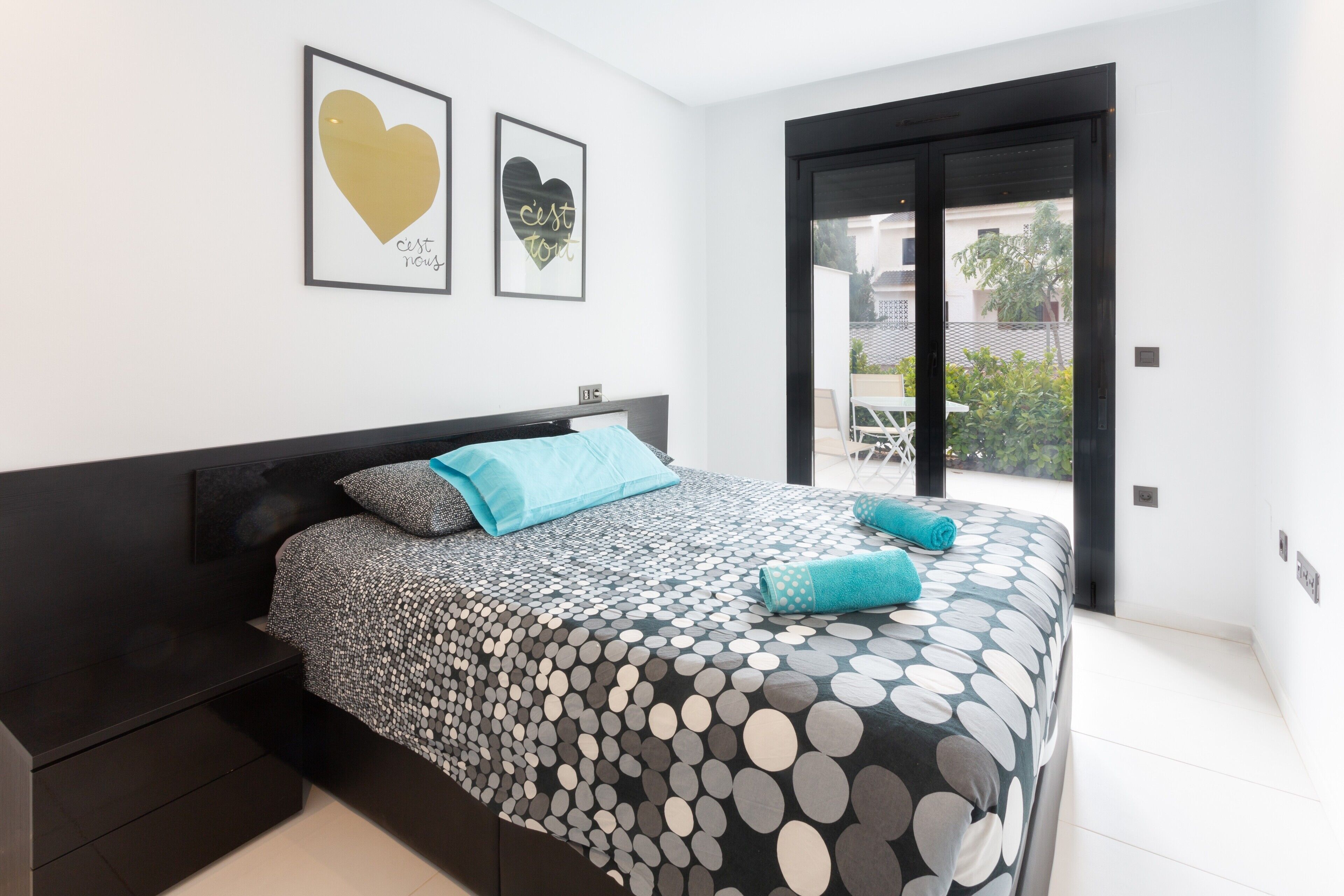 A bedroom with a bed, a nightstand, a window with a view, and two framed pictures on the wall.
