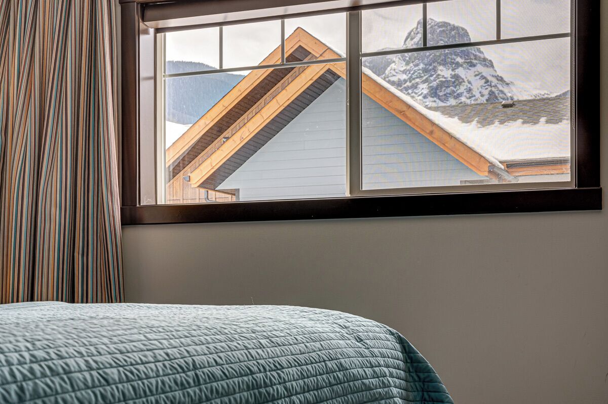 Ein Zimmer mit einem Bett, einem Fenster mit Bergblick und einem gestreiften Vorhang.