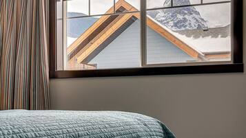 Ein Zimmer mit einem Bett, einem Fenster mit Bergblick und einem gestreiften Vorhang.