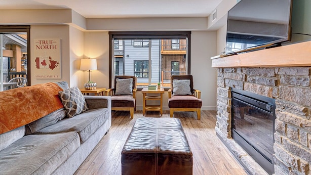 A living room with a fireplace, a sofa, a coffee table, and a TV mounted on the wall. - 3BR, 1250SQFT, NATURE, HOT TUB, KING BEDS, PETS OK (Dead Man's Flats)