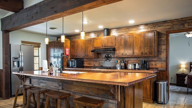 Una cucina con mobili in legno, una grande isola con sgabelli, elettrodomestici in acciaio inossidabile e un soffitto rustico.