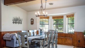 Una sala da pranzo con un tavolo e sedie in legno, un lampadario e ampie finestre con tende.