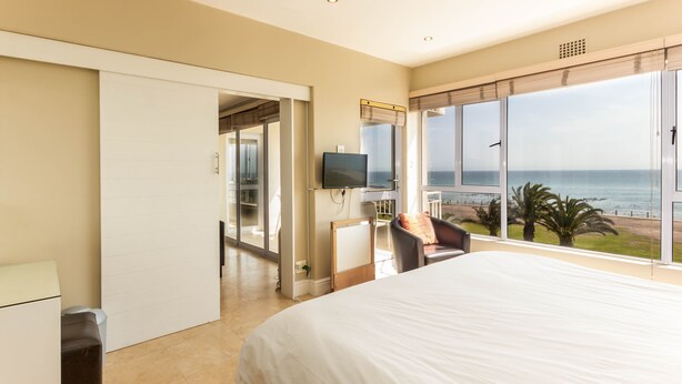A bedroom with a large bed, a TV, a desk, and a view of the ocean.