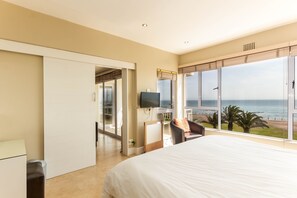 A bedroom with a large bed, a TV, a desk, and a view of the ocean.