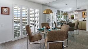 A dining area with a glass table, brown patterned chairs, and a modern pendant light. - Casual Elegance in the Desert | A Louisa Davis Property (Rancho Mirage)