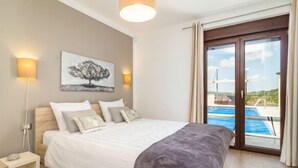 Une chambre à coucher avec un lit, des lampes de chevet, un tableau et une vue sur une piscine.
