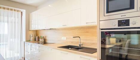 Una cocina moderna con armarios blancos, una encimera negra y electrodomésticos de acero inoxidable, incluyendo un microondas y un horno.