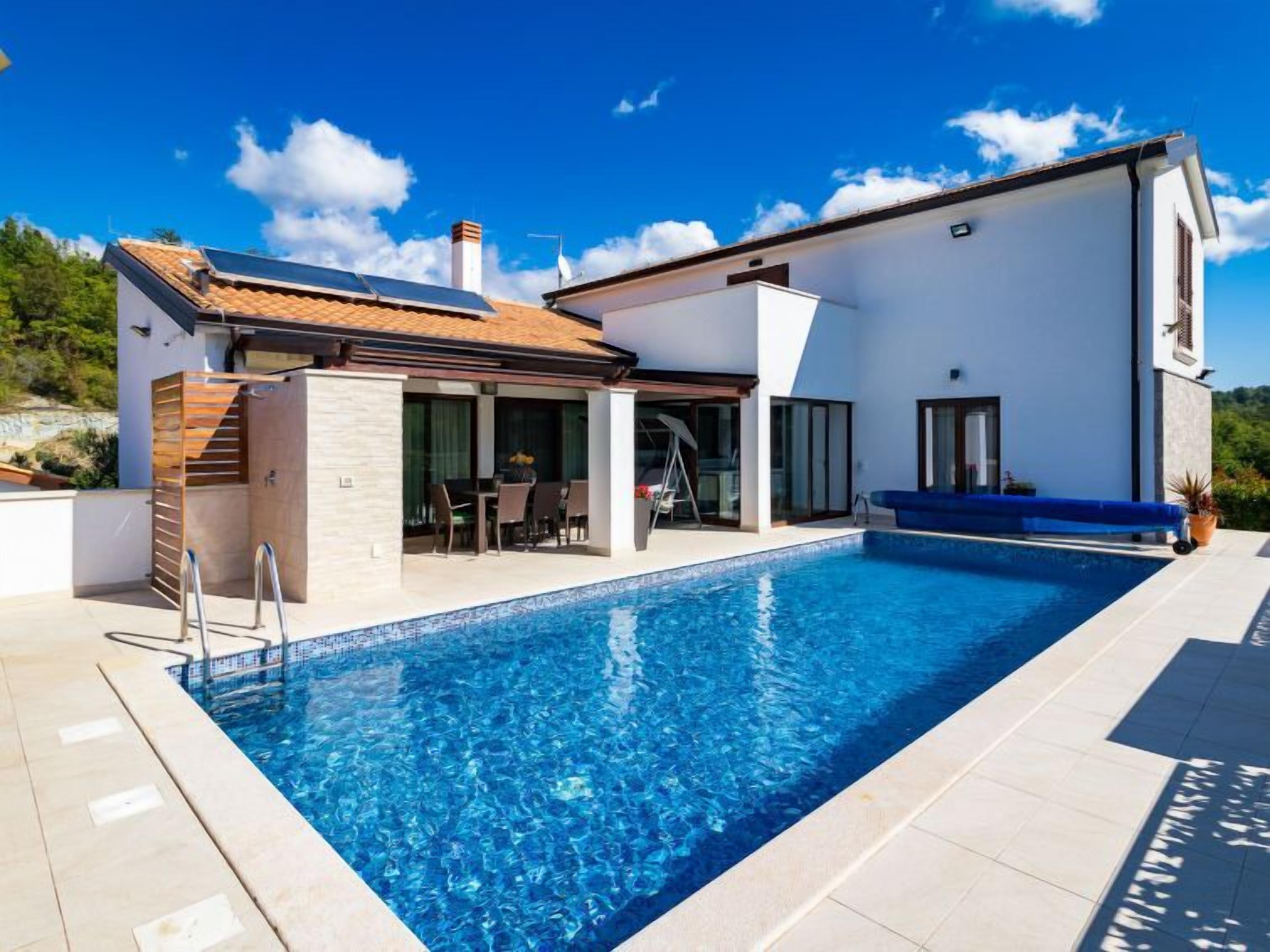 A modern house with a swimming pool, a covered patio, and a view of the surrounding landscape.