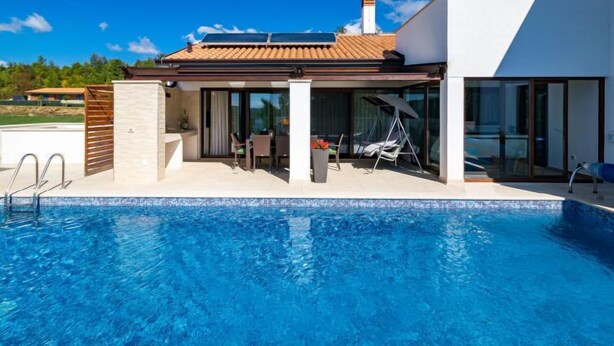 Une maison moderne dotée d’une piscine, d’un patio couvert et d’une grande porte vitrée donnant sur un espace repas.