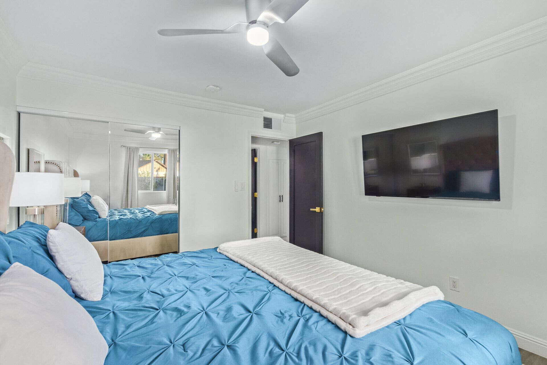 A bedroom with a large bed, a ceiling fan, a window, and a door.