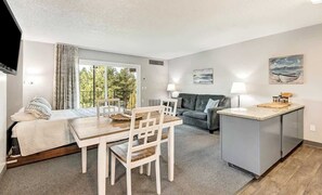 A compact living space with a dining area, a sofa, a small kitchen island, and a TV mounted on the wall.