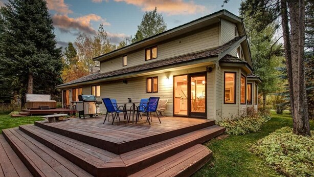 Una casa de dos pisos con terraza, mobiliario exterior y una parrilla.