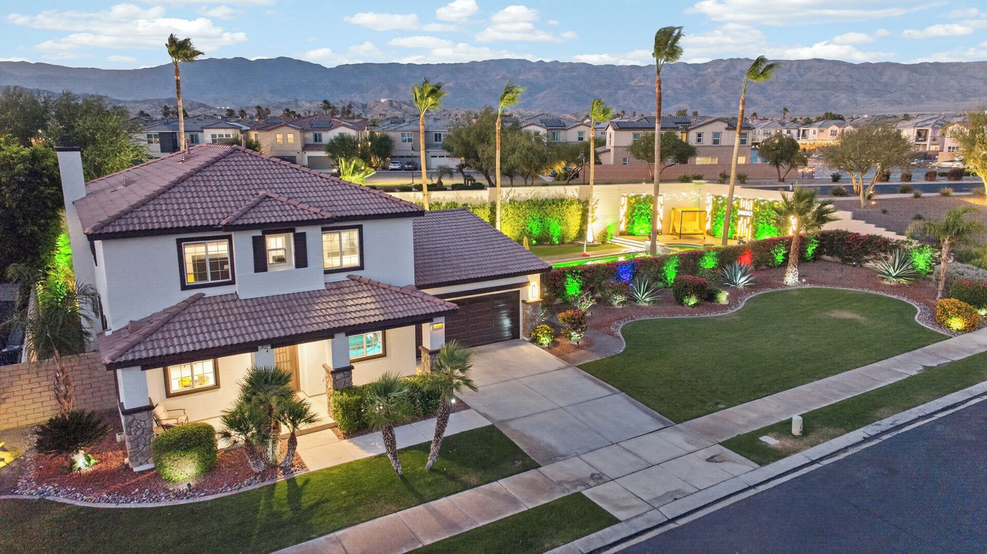 A two-story house with a garage, surrounded by a well-maintained lawn and palm trees.