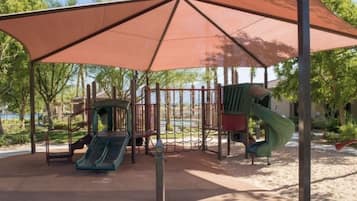 Relax in the shaded seating area, surrounded by trees and a playground with slides and a climbing structure.