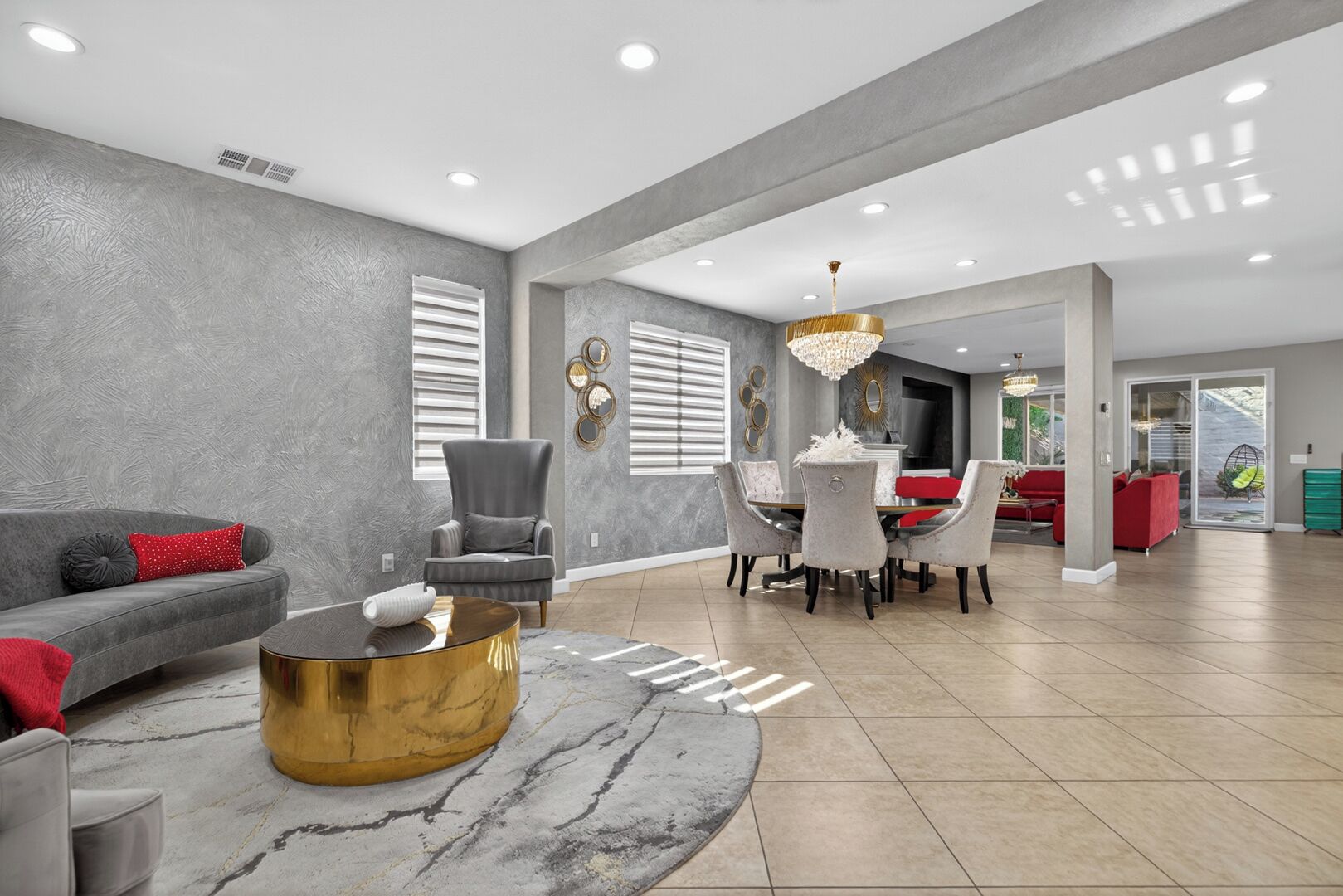 A spacious living area with a grey sofa, a round gold coffee table, and a dining table with chairs.