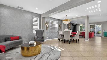 A spacious living area with a grey sofa, a round gold coffee table, and a dining table with chairs.