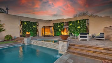 A swimming pool with a fire feature, outdoor seating, and a wall with greenery and butterflies.