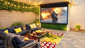Eine Terrassengruppe im Freien mit einer Couch, einem Couchtisch und einem großen Bildschirm, der einen Film zeigt.