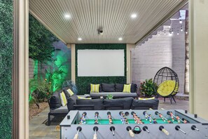 An outdoor seating area with a foosball table, a sofa with cushions, and a chair. - Modern Paradise 15 min 2 Coachella Festival 0.30 acres Lot With misty Huge pool (Indio)