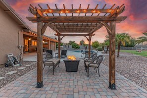 A wooden pergola with string lights, a fire pit, and outdoor seating. - PEACEFUL: One Story, 1 Acre Lot, Htd POOL, Fire Pit, Cornhole, 3 Bikes, TVs All BRs, RV Parking (Mesa)