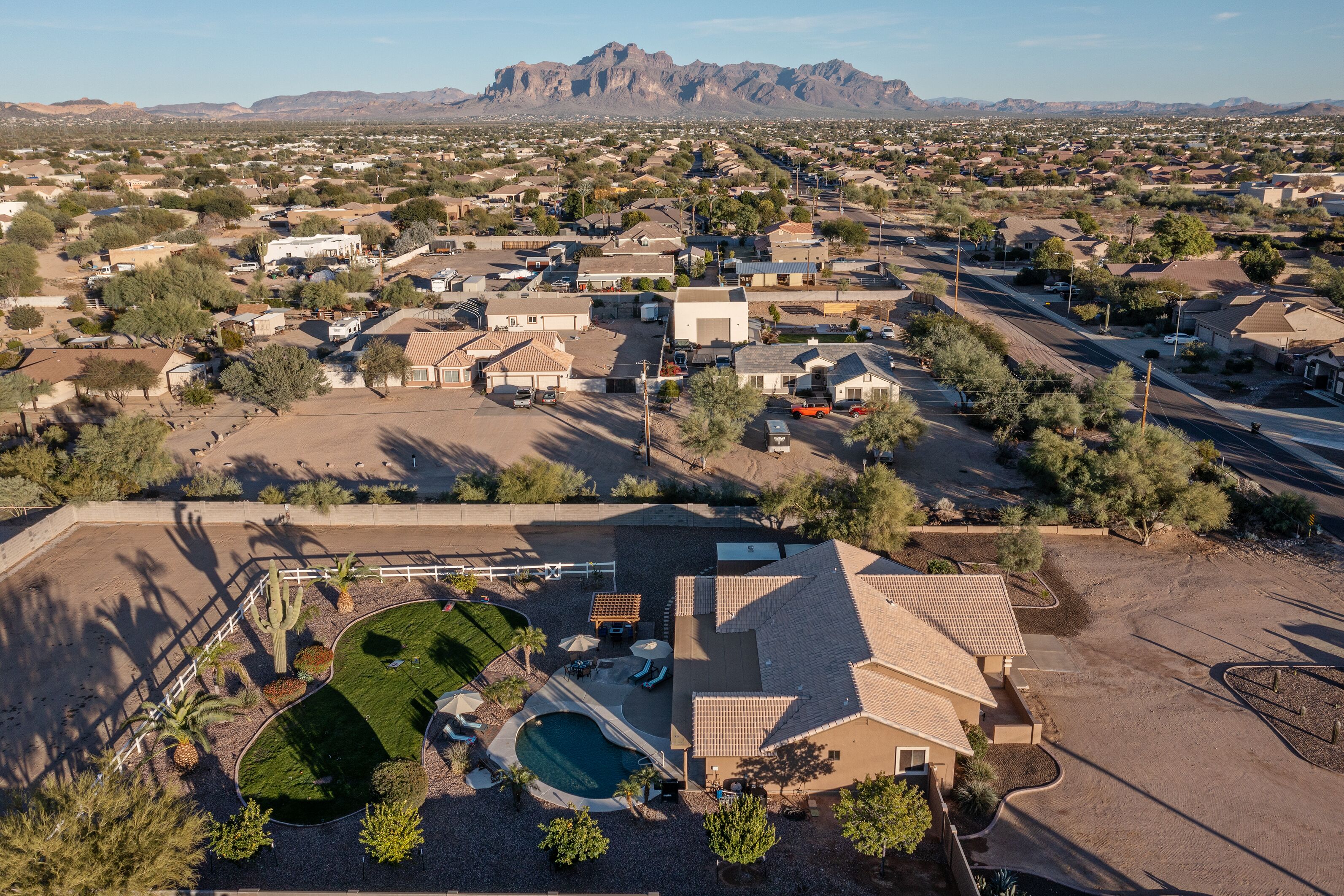 A residential area with a house featuring a swimming pool, a fenced yard, and a mountain view in the background.