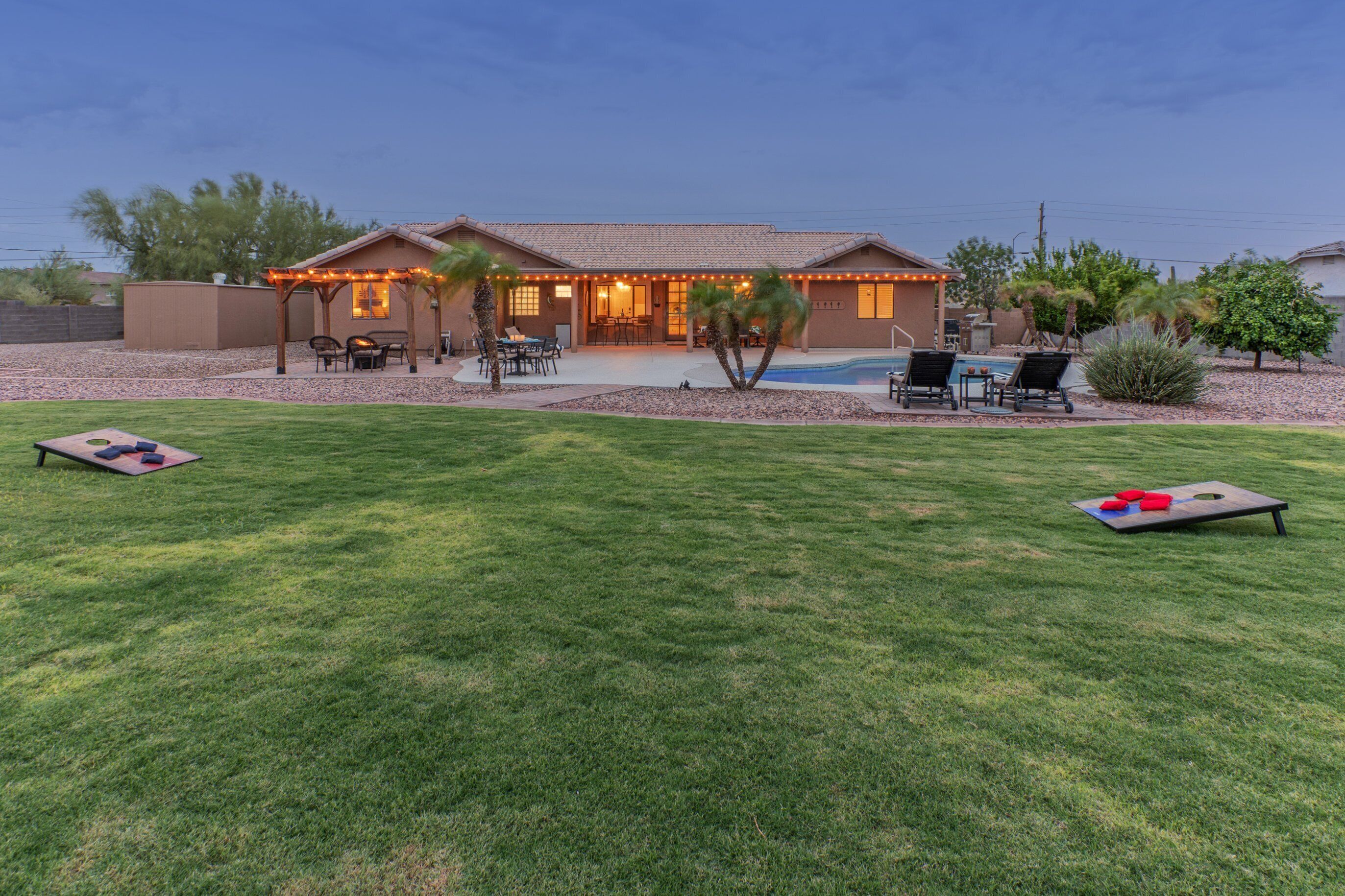 A house with a covered patio, a swimming pool, and a well-maintained lawn.