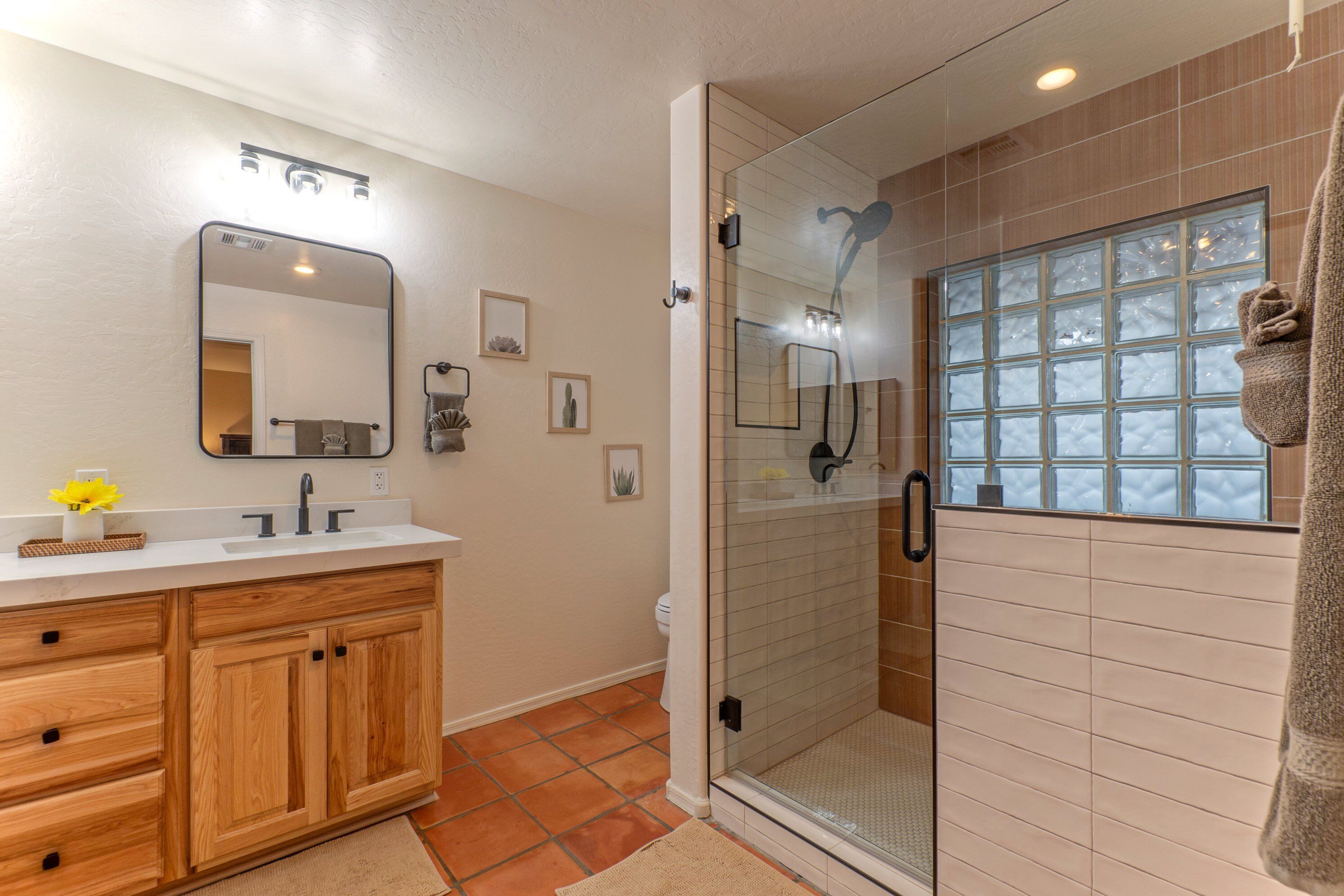 A bathroom with a wooden vanity, a glass shower enclosure, and a window with frosted glass.