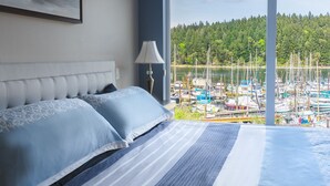 A bedroom with a bed, a lamp, and a view of a marina with boats. - This is the life! 2 bedroom oceanfront condo close to everything. (Nanaimo)