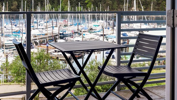 A covered outdoor seating area with a table and chairs, overlooking a marina with numerous boats. - This is the life! 2 bedroom oceanfront condo close to everything. (Nanaimo)