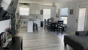 Une cuisine moderne avec des meubles blancs, un coin repas doté d’une table et de chaises noires, et un canapé gris.