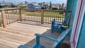 Une terrasse en bois avec deux chaises Adirondack bleues et un tapis aux couleurs vives.