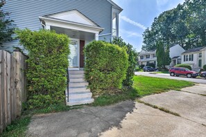 Two-story house with a front porch and steps leading to the entrance, surrounded by a fence and lush greenery.