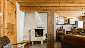 Een gezellige woonkamer met een open haard, houten meubels en een keuken op de achtergrond.