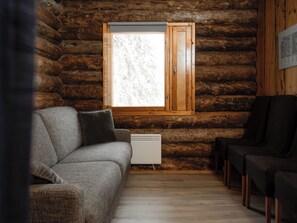 A log cabin interior with a sofa, a radiator, and a window with a view of trees. - Napakymppi by Interhome (Kuusamo)