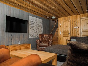 A cozy living room with a flat-screen TV, a patterned wall hanging, a leather armchair, a sofa, and a wooden staircase. - Napakymppi by Interhome (Kuusamo)