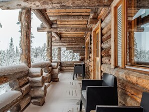 A log cabin with a covered porch, wooden walls, and a view of snow-covered trees. - Napakymppi by Interhome (Kuusamo)