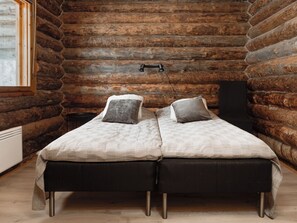 A log cabin room with a double bed, pillows, a small table, and a window. - Napakymppi by Interhome (Kuusamo)