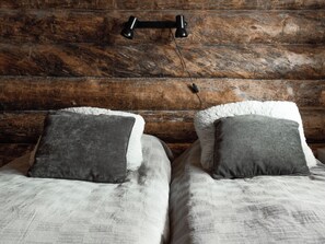 A rustic wooden cabin interior with two beds, each with a grey pillow and a white fluffy throw. - Napakymppi by Interhome (Kuusamo)