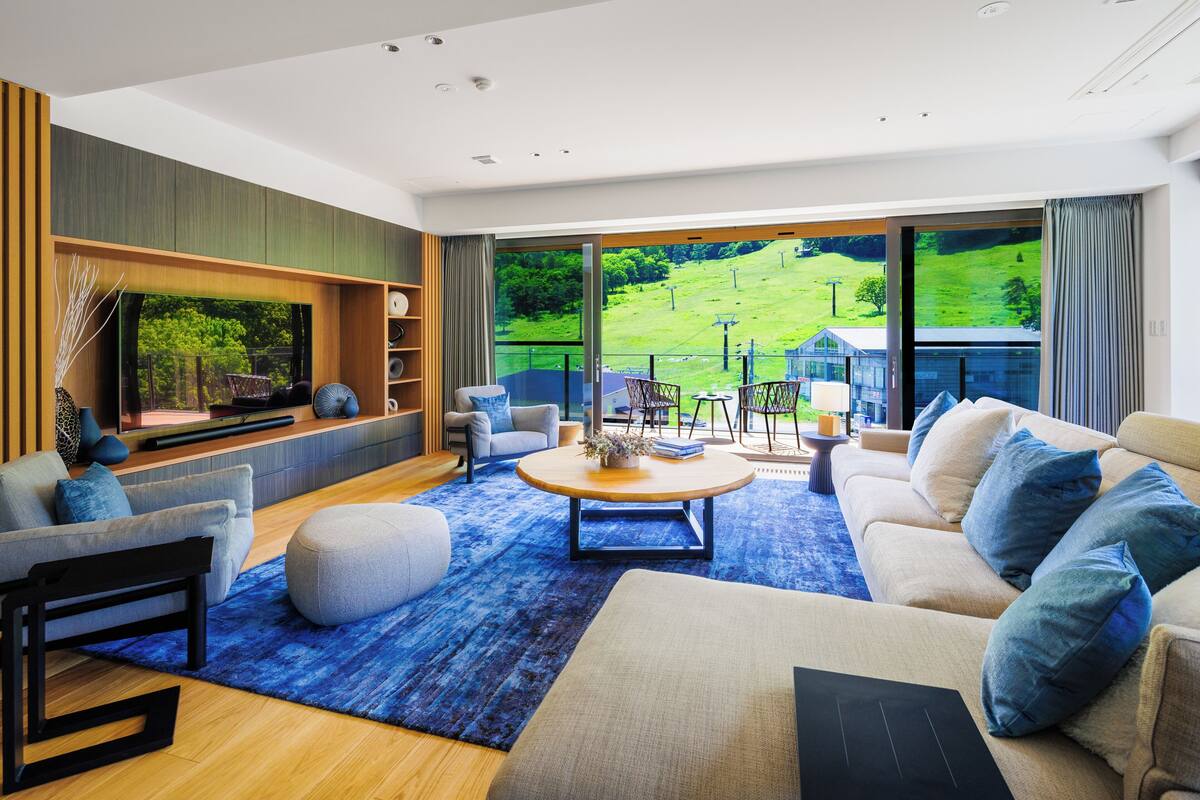 A modern living room with a large window, a sofa set, a coffee table, and a bookshelf.